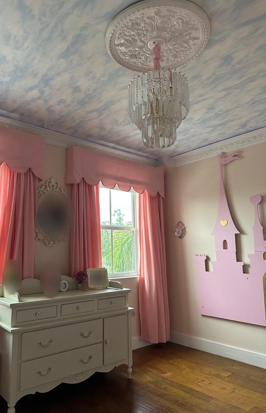 Cuarto infantil con techo pintado de nubes, cortinas rosadas y un castillo de madera rosado montado en la pared